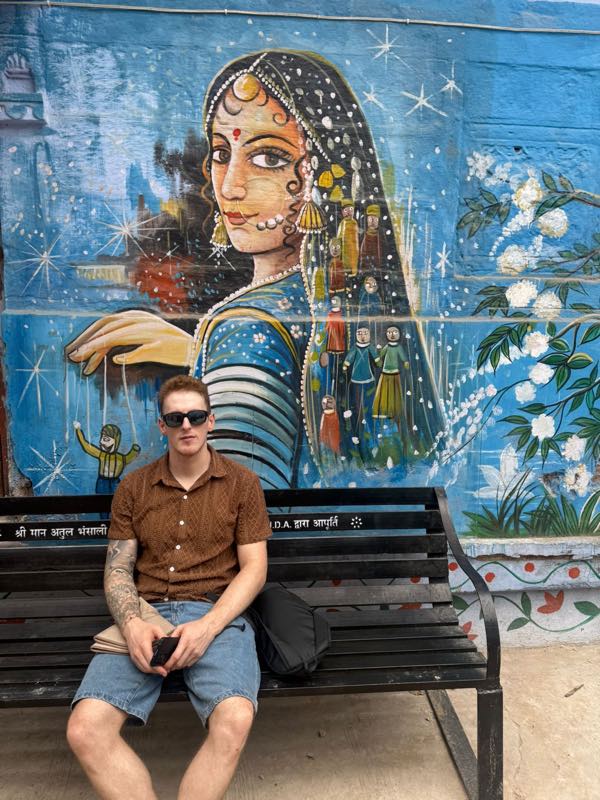 A guest on a painted bench below a Rajasthani mural